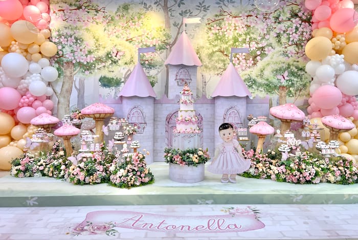 Cenário de festa infantil com castelo cenográfico, flores, balões e mesa de doces