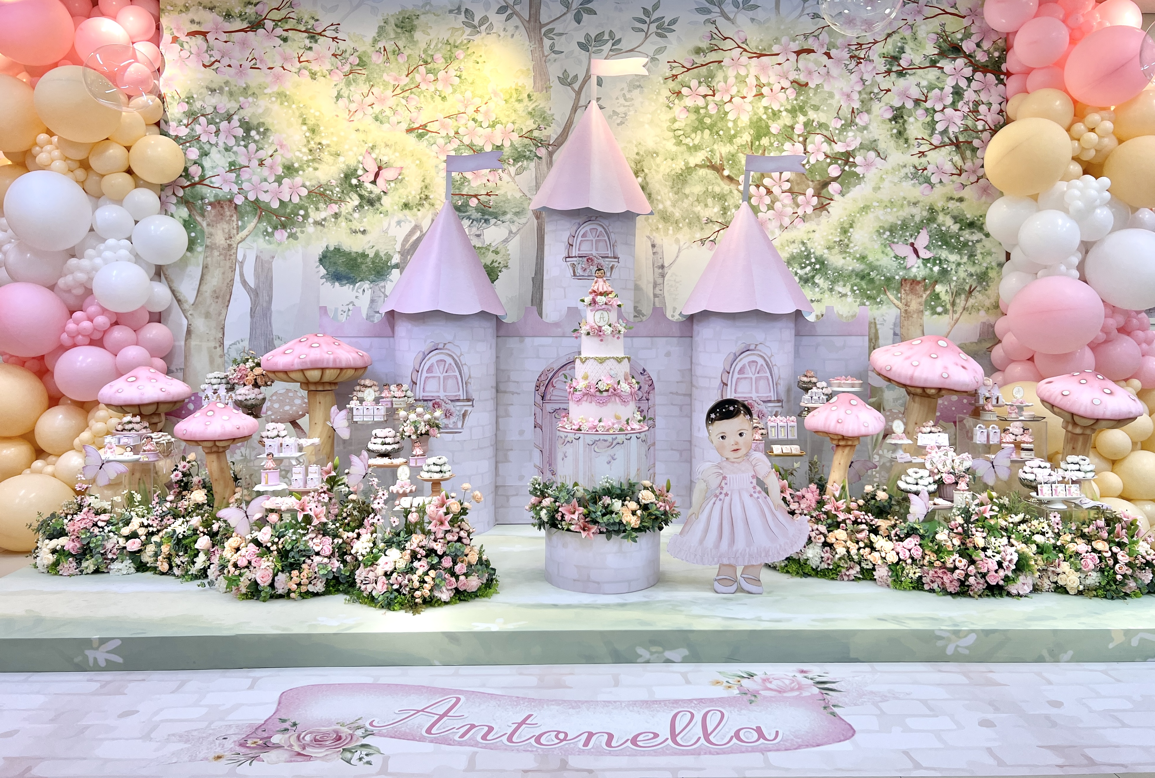 Cenário de festa infantil com castelo cenográfico, flores, balões e mesa de doces